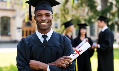 Happy graduate. Happy African man in graduation gowns holding diploma and smiling while his friends standing in the background
